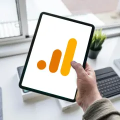 Ręka trzyma tablet z ikoną Google Analytics 4. Analiza zdarzeń GA4 na urządzeniu mobilnym.