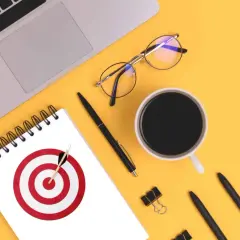 Na biurku leżą laptop, okulary, kubek kawy i notatnik z tarczą strzelniczą. To inspiracja, jak stworzyć personę.