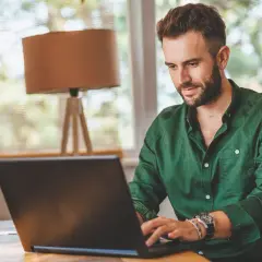 Mężczyzna w zielonej koszuli pracuje przy laptopie, tworząc **lead artykułu** o pracy zdalnej.