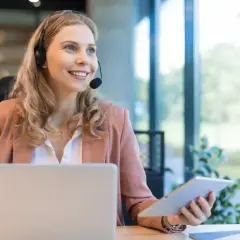 Uśmiechnięta konsultantka z branży SEO, pracująca przy laptopie i tablecie, z zestawem słuchawkowym na głowie.