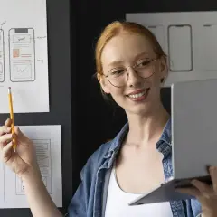 Kobieta z rudymi włosami i okularami omawia projekty interfejsów aplikacji, skupiając się na ux writing.