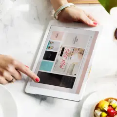 Kobieta przegląda tablet z ofertami, szukając inspiracji, jak zarabiać na reklamach. Obok deser i napój.