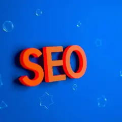 Pomarańczowe litery SEO unoszą się na niebieskim tle, otoczone bańkami i gwiazdkami. Kluczowe słowa dla Twojej strony.