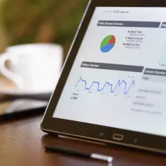 Tablet z wykresami ruchu na stronie, pokazujący dane do promowania strony w Google. Obok filiżanka kawy.