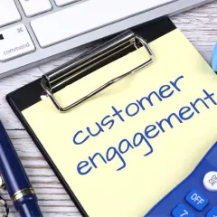 Notatka z napisem "customer engagement" obok klawiatury, długopisu i kalkulatora.