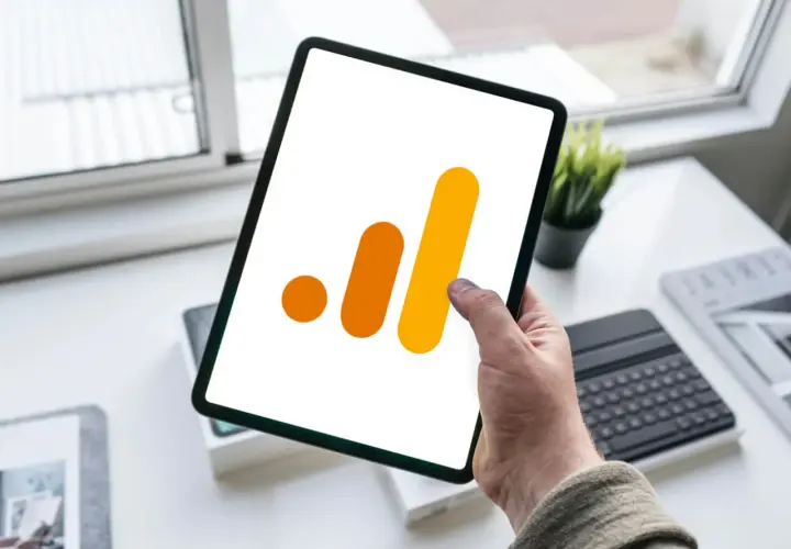 Ręka trzyma tablet z ikoną Google Analytics 4. Analiza zdarzeń GA4 na urządzeniu mobilnym.