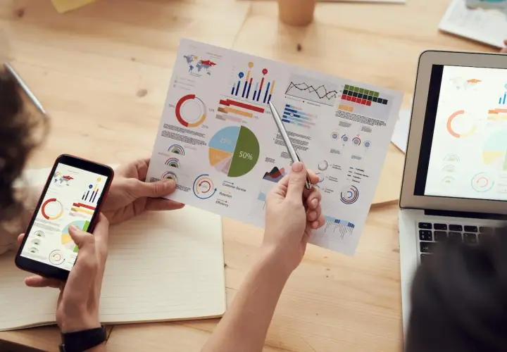 Analiza danych z Yandex Metrica na papierze i ekranie telefonu. Wykresy i diagramy kołowe pokazują kluczowe wskaźniki.