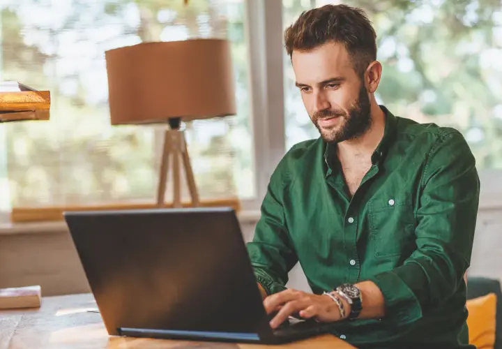 Mężczyzna w zielonej koszuli pracuje przy laptopie, tworząc **lead artykułu** o pracy zdalnej.