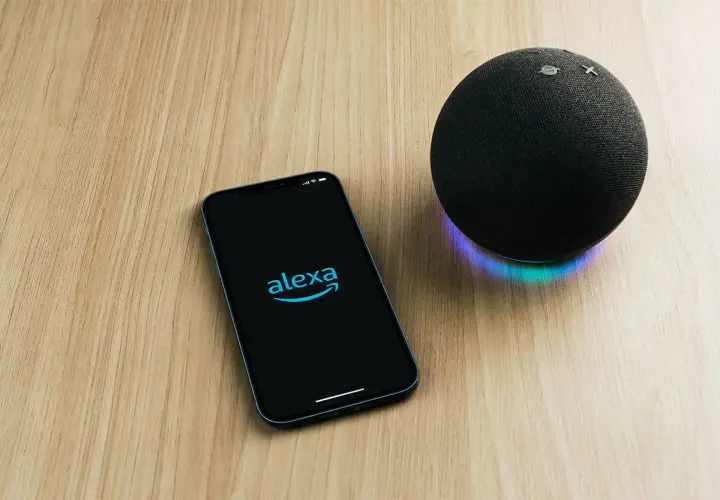 Telefon z logo Alexa i głośnik Echo na drewnianym blacie. Chcesz wiedzieć, alexa co to?