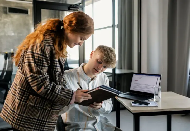 Dwóch młodych ludzi analizuje dokumenty, planując strategię multi channel marketing. Na biurku laptop, telefon i notatnik.
