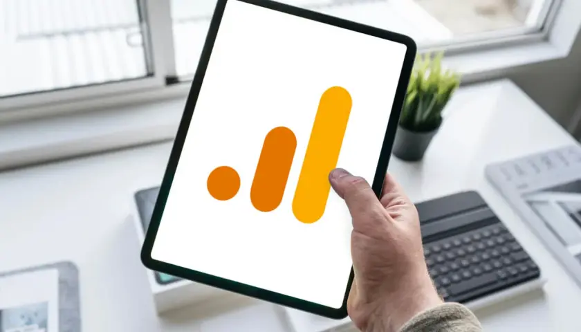Ręka trzyma tablet z ikoną Google Analytics 4. Analiza zdarzeń GA4 na urządzeniu mobilnym.