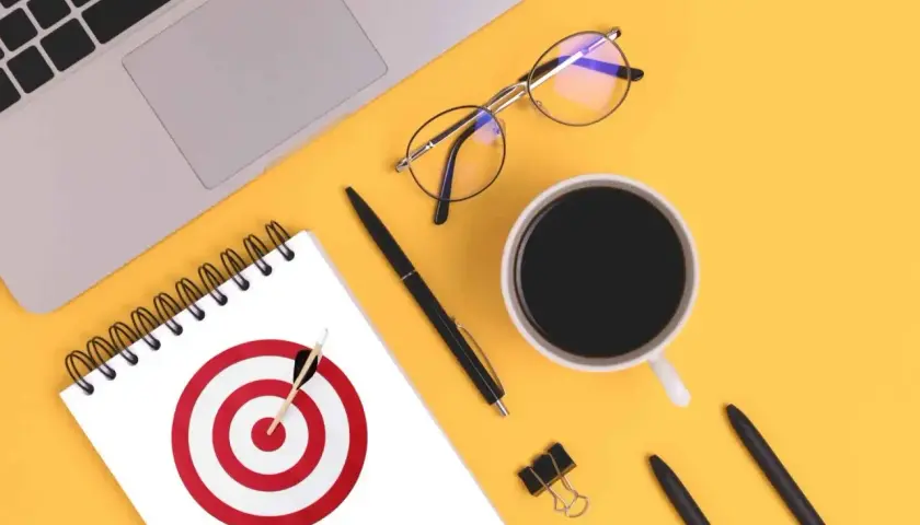 Na biurku leżą laptop, okulary, kubek kawy i notatnik z tarczą strzelniczą. To inspiracja, jak stworzyć personę.