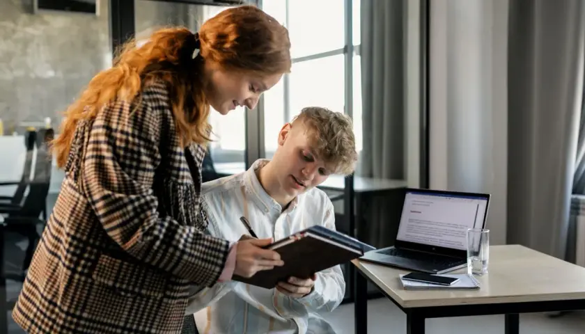 Dwóch młodych ludzi analizuje dokumenty, planując strategię multi channel marketing. Na biurku laptop, telefon i notatnik.