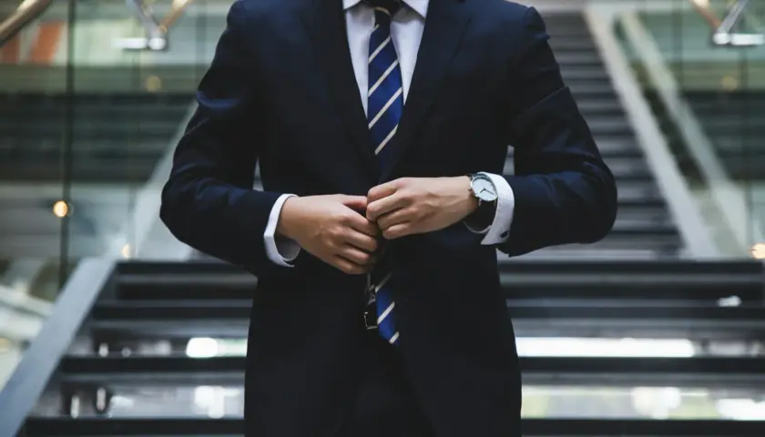 Elegancki mężczyzna w garniturze, zapięty pod szyją, z zegarkiem na ręku, gotowy do roli ambasadora marki.