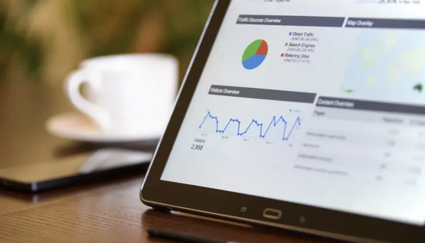 Tablet z wykresami ruchu na stronie, pokazujący dane do promowania strony w Google. Obok filiżanka kawy.