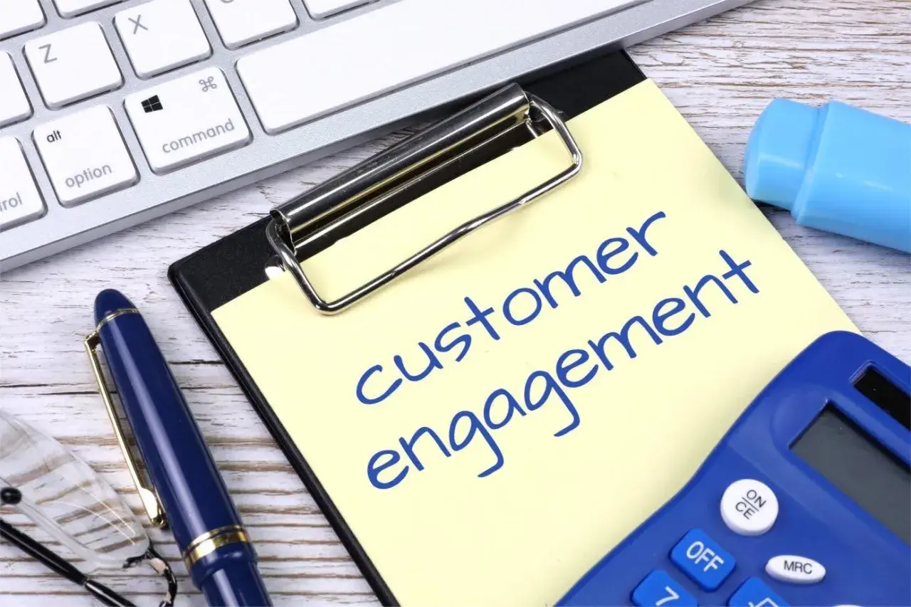 Notatka z napisem "customer engagement" obok klawiatury, długopisu i kalkulatora.
