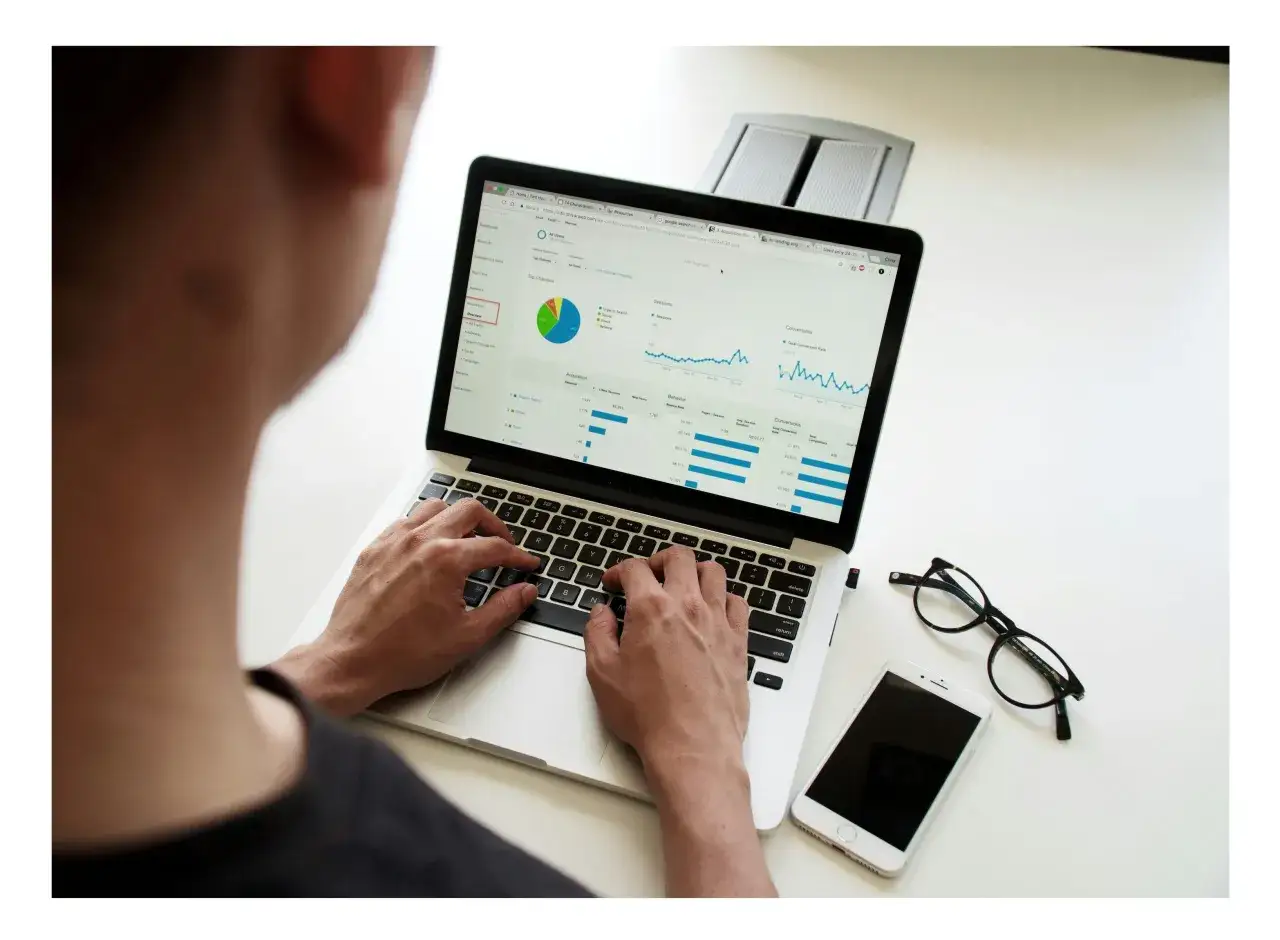 Osoba analizuje dane na laptopie, szukając sposobów na poprawę wyników, być może unikając negatywnego SEO. Obok leżą okulary i smartfon.