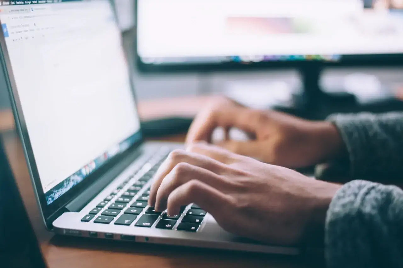 Dłonie piszą na klawiaturze laptopa, tworząc nowy wpis na bloga.