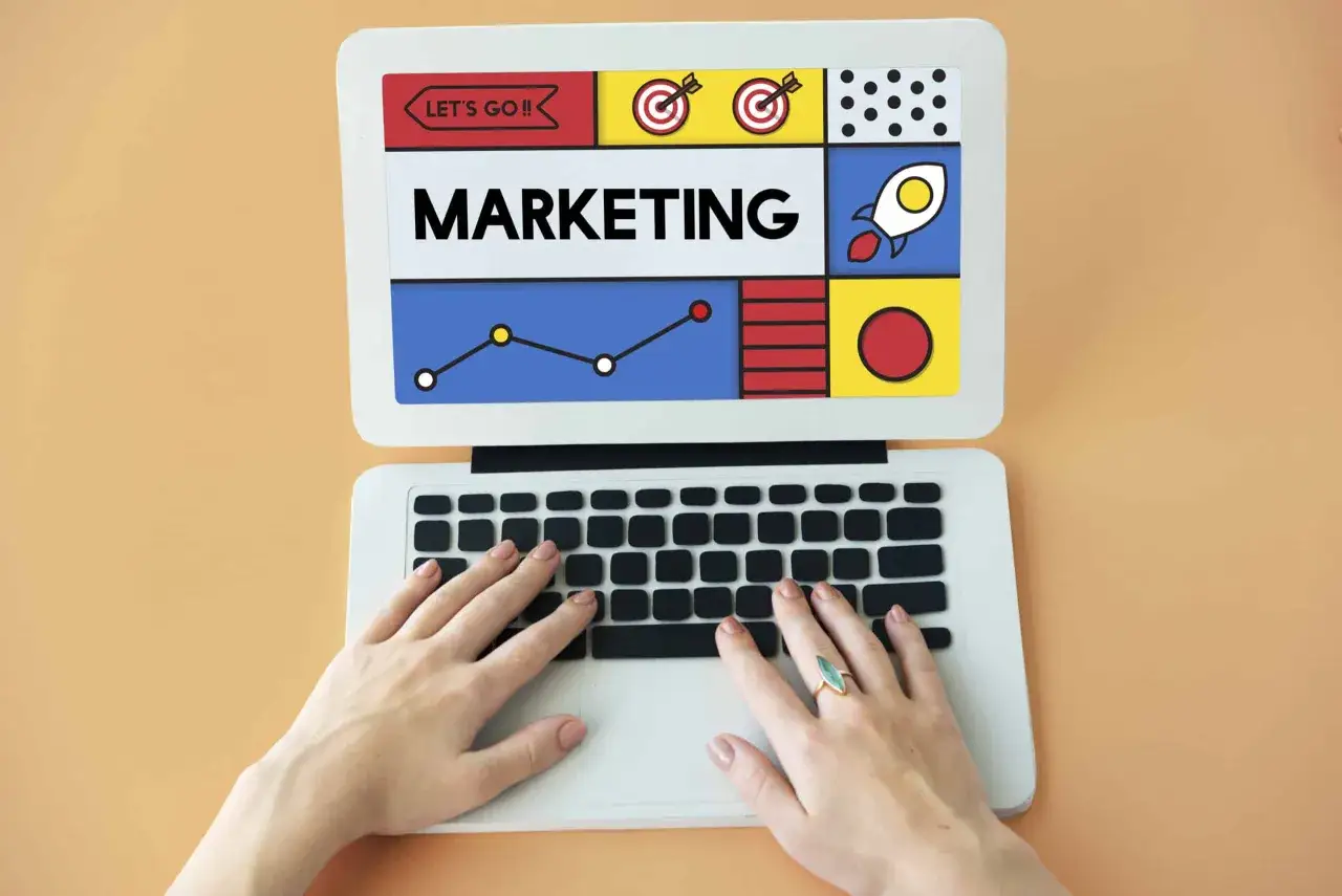 Ręce na klawiaturze laptopa, na ekranie napis MARKETING i grafiki symbolizujące sukces. Pamiętaj, że content is the king!